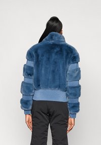 Casaco de pele sintética azul com um design de suéter de malha canelada. Apresenta um colarinho alto e detalhes de pelagem riscada nas mangas e nas costas.