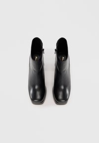 Pár černých kožených kotníkových bot se bočními zipy, čtveratými špičkami a nízkými blokovými podpatky na bílém pozadí.