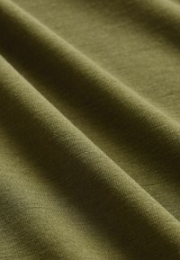 Olivgrön tyg med en mjuk, texturerad yta, som har en lätt lyster och en synlig vävstruktur, hängande i mjuka veck.