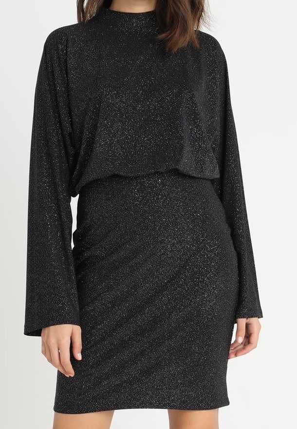 Robe noire à manches longues pailletée avec un col haut, une taille cintrée et des manches légèrement évasées portée par une personne debout.