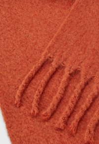 Écharpe en laine orange brûlé à texture douce avec des franges à une extrémité, présentée sur une surface blanche.