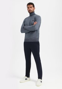 Grijze coltrui met een gestructureerde brei, gecombineerd met navy slim-fit broek en witte sneakers met navy accenten.