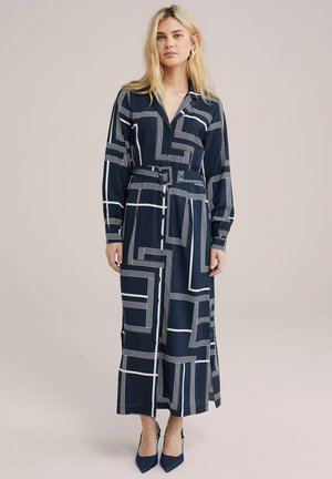 Lange marineblauwe jurk met witte geometrische patronen, met een kraag, knopen aan de voorkant, een ceintuur in de taille en lange mouwen.