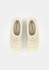 Zapatos beige acolchados tipo slip-on con suela de goma blanca, con cierre de cordón ajustable y forro suave. Logo de Columbia visible en la plantilla.
