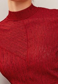 Top rosso realizzato in tessuto testurizzato, caratterizzato da strisce verticali e a chevron, con un design a collo alto e modelli a contrasto nel materiale.
