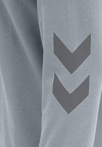 Sudadera azul claro con un tejido texturizado y un prominente diseño en forma de chevron gris en la manga izquierda.