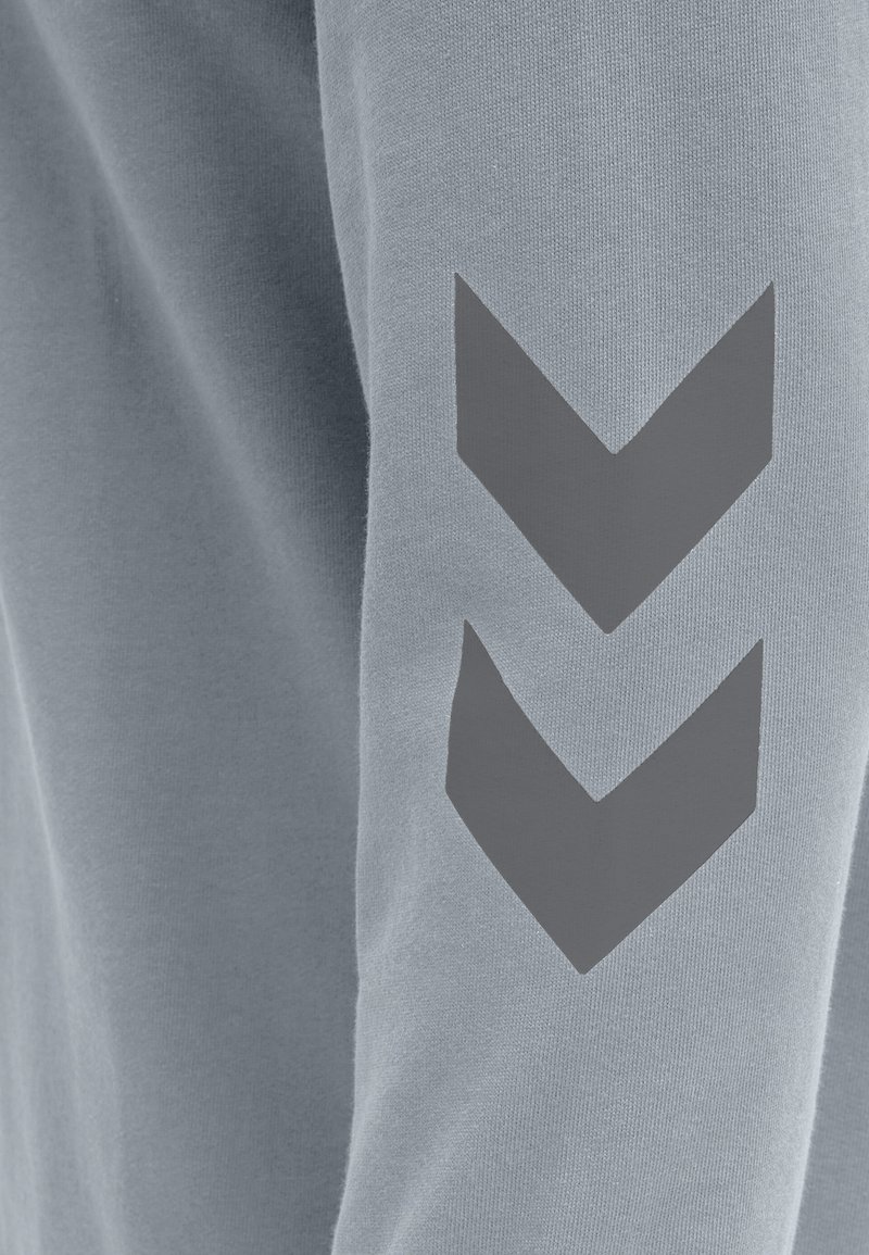 Hellblaues Sweatshirt mit strukturiertem Stoff und einem auffälligen grauen Chevron-Design am linken Ärmel.