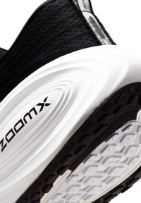 Tomaia in tessuto nero con suola in gomma bianca e nera. Presenta il marchio "zoomx" e una superficie testurizzata sulla suola con un motivo geometrico.