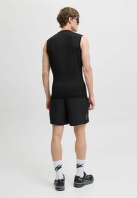 Mustamata varrukateta spordisärk, mis on kombineeritud mustade lühikeste pükstega. Pükste tekstureeritud kangas ja peegeldavad detailid. Mustad spordijalatsid ja mustrilised sokid.