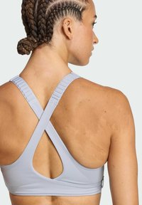 Light gray sports bra with crossed back straps, elastic material, and cutout detailing. Features textured strap adjustments.