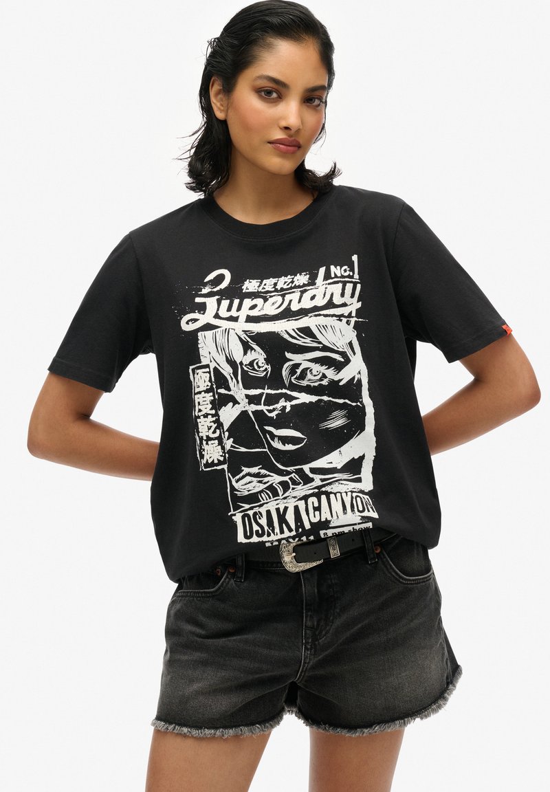 T-shirt nera in cotone con stampa grafica bianca di un volto e testo. Abbinata a pantaloni corti in denim scuri con bordi sfrangiati.