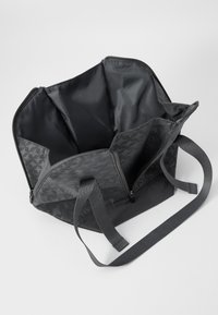 Svart stoff tote bag med et hundetannmønster, med en bred åpning, to stropper og flere rom inni.