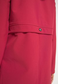 Giacca rosa brillante con una texture liscia, una vestibilità aderente e un dettaglio decorativo con bottone in vita, caratterizzata da un design con cuciture sottili.