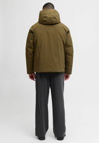 Olivgrüne Steppjacke mit hohem Kragen, sichtbaren Nähten und lockerem Schnitt. Kombiniert mit grauen, weitem Hosenbein.