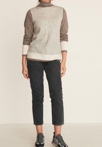 Gray and brown color-block sweater with a mock neck, ribbed cuffs, and hem, paired with black jeans and patterned sneakers.