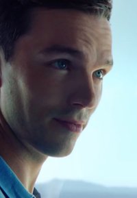 Gros plan sur le visage d'une personne avec des cheveux châtain clair, des yeux bleu clair, une peau claire et d'une texture lisse, portant un vêtement bleu.