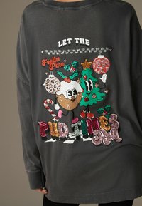 Graues Langarmshirt mit bunten, glitzernden Cartoon-Figuren, Text und festlichen Elementen wie einem Weihnachtsbaum und Ornamenten.