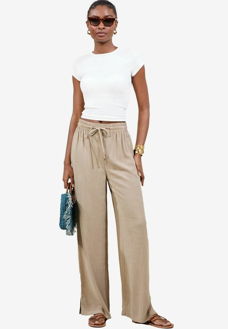 Pantaloni beige a gamba larga con vita regolabile, abbinati a un top bianco aderente. Accessoriati con una borsa in franbo turchese e sandali marroni.