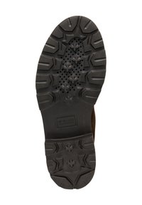 Suela de zapato de goma negra con patrones de agarre texturizados y agujeros de drenaje, que presenta un área de talón suave y curvada y un logo de marca rectangular.