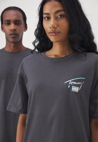 Camisetas de algodón gris con mangas cortas, que presentan un colorido logo de "Tommy" en el pecho. Textura suave, corte relajado y diseño de cuello redondo.