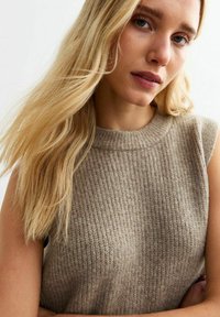 Beige ribbad ärmlös tröja med hög hals, tillverkad av en mjuk ullblandning, med ett texturerat mönster och minimalistisk design.