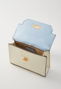 Sac à main en cuir beige avec rabat bleu clair ouvert, montrant une fermeture dorée et une poche intérieure zippée sur un fond clair uni.