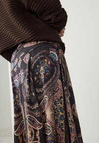 Jupe sombre à motifs floraux bleus, roses et jaunes sur fond noir. Fabriquée en tissu léger et texturé.