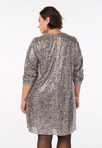 Abito a maniche corte, lungo fino al ginocchio, realizzato in tessuto a maglia testurizzata nei toni del bronzo metallico e dell'argento. Presenta un'apertura a chiave sul retro e una vestibilità morbida.