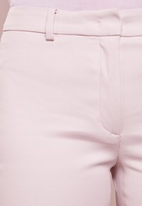 Jasnoróżowe spodnie o dopasowanym kroju, wykonane z teksturowanej tkaniny, z gładkim wykończeniem, szlufkami na pasek oraz bocznymi kieszeniami z czystymi detalami w szyciu.