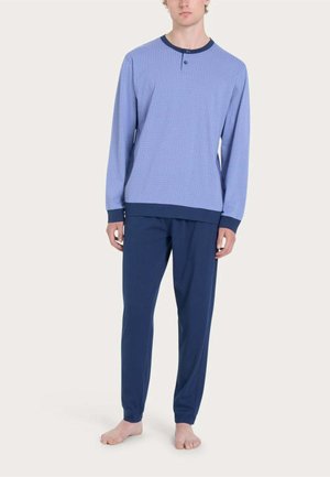 Modello maschile indossa una maglia a manica lunga azzurro chiaro fantasia con colletto e polsini blu navy, pantaloni blu navy, in piedi a piedi nudi su sfondo semplice.