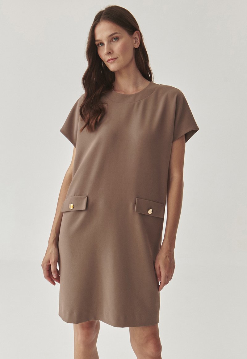 Brown short-sleeve dress featuring a round neckline and two front pockets with gold buttons. Smooth fabric, loose silhouette, above-knee length.
