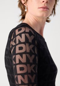 Schwarzes Netzoberteil mit einem auffälligen, sich wiederholenden "DKNY"-Muster, passgenauer Schnitt und langen Ärmeln. Akzentuiert mit durchscheinendem Stoff und Ausschnitt.