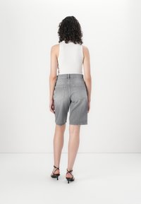 Grå denimshorts med høy midje, frynsete kant og to baklommer, sammen med en hvit ermeløs topp og svarte sandaler med stropper.