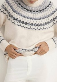 Maglione lavorato a maglia di colore crema con un motivo a yoke grigio e blu scuro, dotato di polsini e orlo a coste. Abbinato a pantaloni bianchi a coste.