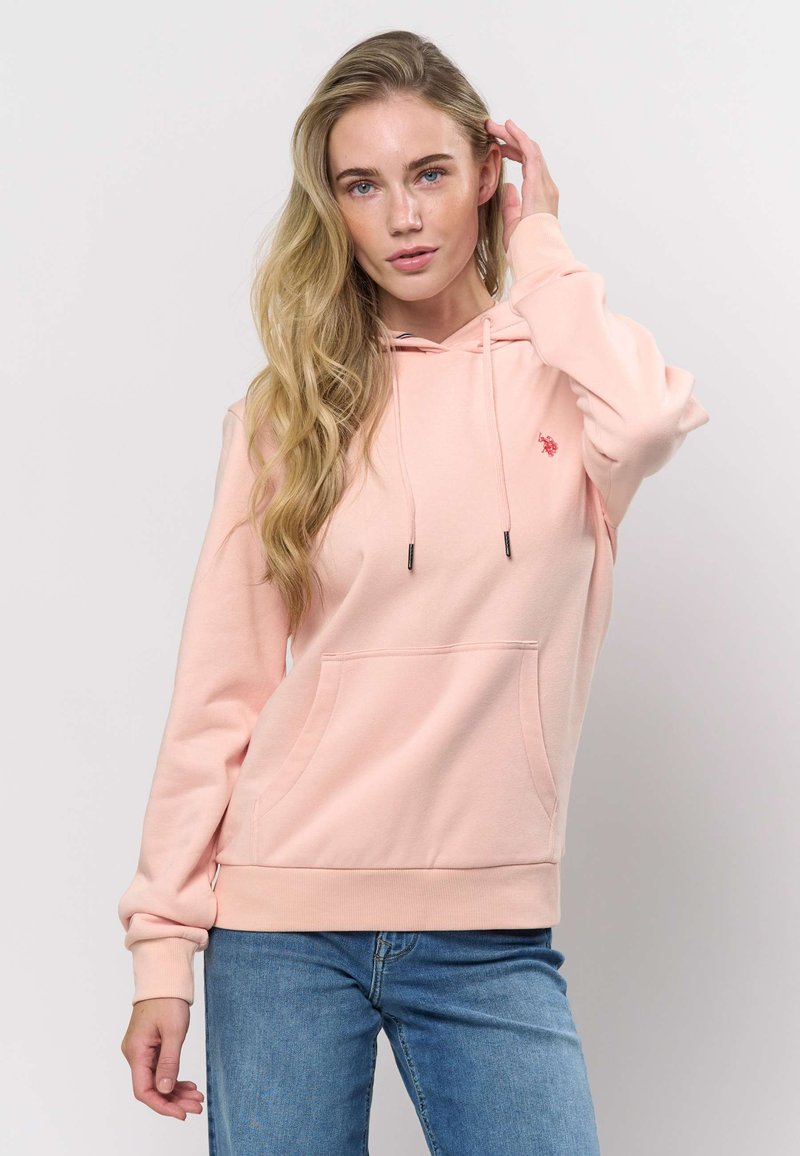 Roza bombažna jopa z žepom na sprednji strani, kapuco z zateznim trakom in rebrastimi manšetami. Na prsih je majhen logotip. Oblečeno skupaj z modrimi kavbojkami.