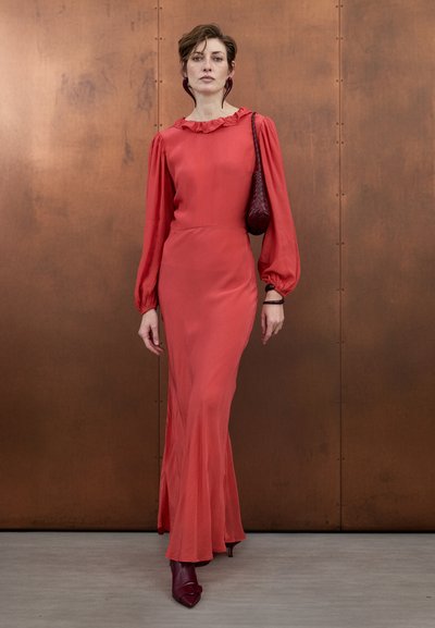 Raudona, ilgarankovė suknelė su raukšlėtu iškirpimu, laisvu siluetu ir aptemptu liemeniu. Derinama su bordo spalvos aukštakulniais aulinukais ir austu rankinės.