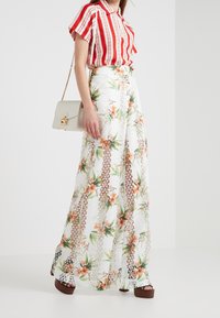 Pantalones de pierna ancha blancos con un diseño de malla en capas; combinados con una camisa de manga corta a rayas rojas y blancas y un bolso color crema.