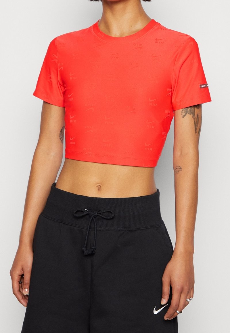 Rotes, tailliertes Nike-Sport-T-Shirt mit eingeprägtem Logo-Design; kurze Ärmel und runder Ausschnitt; getragen mit schwarzen Sweatpants mit Kordelzug.