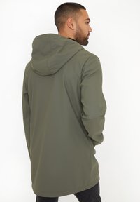 Veste à capuche vert olive en matériau lisse et résistant à l'eau, avec une coupe décontractée et un dos plus long. Design simple sans embellissements visibles.