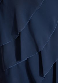 Tela de gasa en azul marino en capas con volantes ondulados, que presenta una textura suave y un delicado detalle de costura a lo largo de los bordes.