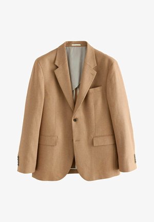 Persoon die de manchetknoopjes van een beige maatpak aanpast, met vier donkere knopen en een gestructureerde stof.