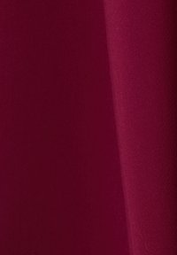 Burgundská látka má hladkou texturu s matným povrchem. Materiál působí lehce a jemně se splývá, což zdůrazňuje jeho tekutost.
