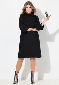 Vestido negro con cuello cisne, diseño floral bordado, mangas tres cuartos y un corte relajado, combinado con botas metálicas hasta el tobillo.