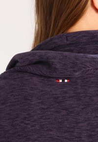 Maglione navy con una superficie morbida e testurizzata e un piccolo logo ricamato in rosso, bianco e nero sul retro vicino al colletto.