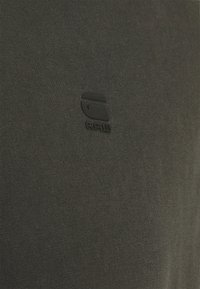 Camiseta de color gris oscuro hecha de un suave material de algodón, con un logo negro texturizado "RAW" en el frontal. Diseño simple y minimalista.
