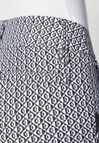 Pantaloni corti in bianco e nero con un motivo geometrico di triangoli intrecciati e lettere, con un dettaglio di metallo vicino alla vita.