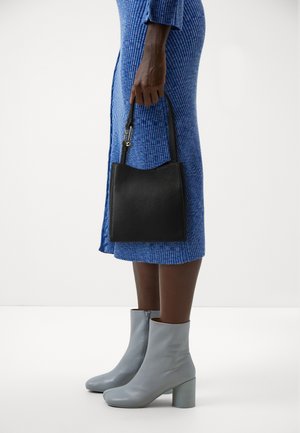 Czarna torebka skórzana o teksturowanej powierzchni z zaokrąglonym dnem, trzymana przez osobę ubraną w niebieską sukienkę z prążkowanym wzorem oraz szare botki za kostkę na grubych obcasach.