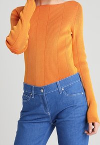Ribbed orange pitkähiha toppi, jossa on neliönmuotoinen pääntie, yhdistettynä sinisiin farkkuihin, joissa on tiukka leikkaus ja klassinen viisi taskua.