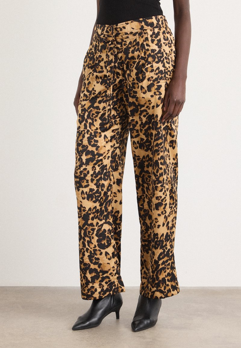 Femme portant un pantalon taille haute à jambes larges avec un imprimé léopard beige et noir, associé à des bottines à talons pointues noires.