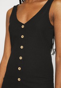 Μαύρο ριγέ φόρεμα χωρίς μανίκια με βαθύ V-λαιμόκοψη και έξι ξύινους κουμπίδες μπροστά. Λείο υλικό και εφαρμοστό σχήμα.